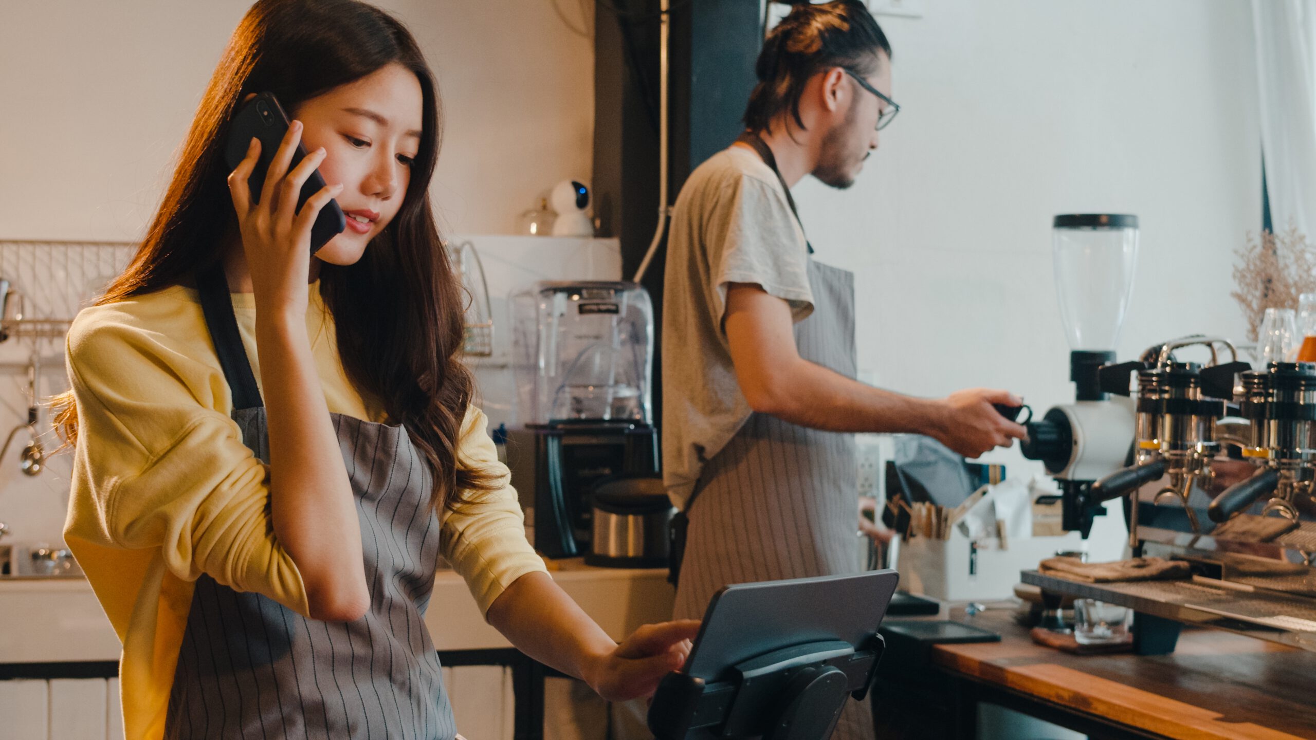 Barista taking a phone order while a coworker prepares coffee at the espresso machine